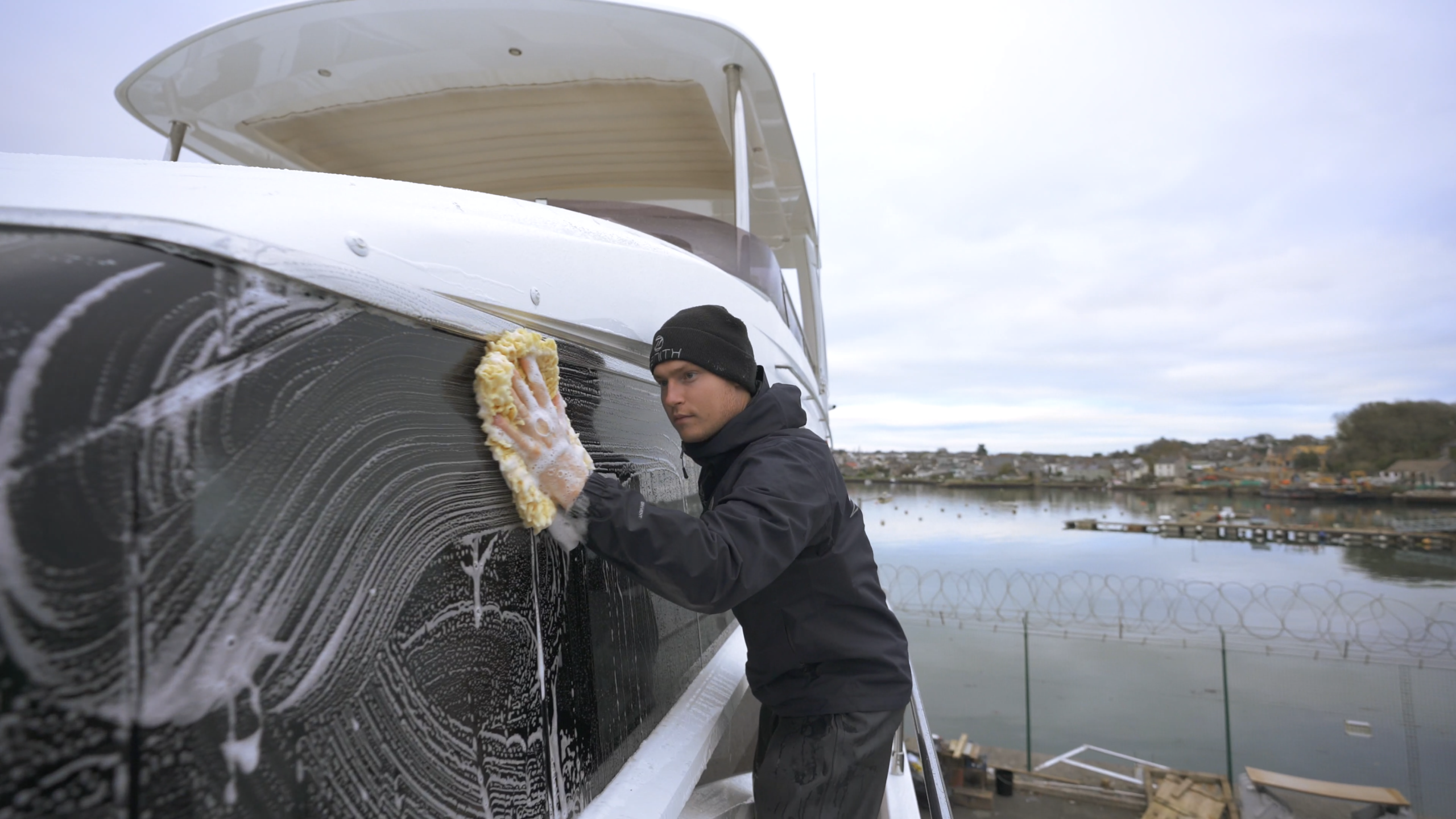 Crew member carrying out exterior yacht washdown at marina